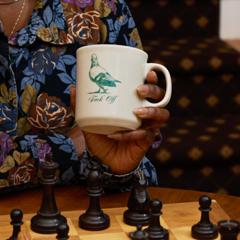 Person holding a mug with a duck design over a chessboard